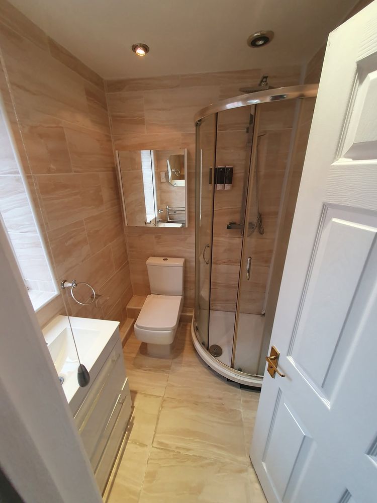 Compact bathroom with curved shower enclosure and beige tiles