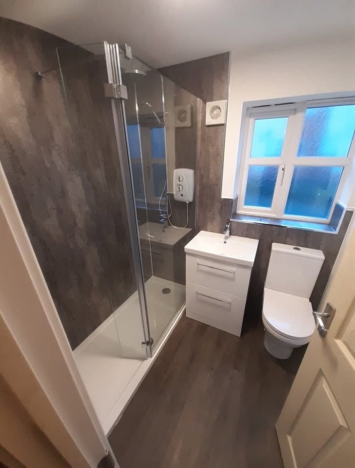 White vanity and toilet with dark grey tiles and glass shower